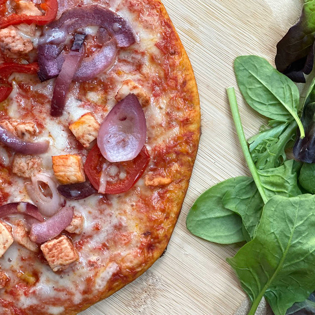 Picture - Close up photo of a cooked keto chicken pizza showcasing the chicken chunks, onion & pepper. 