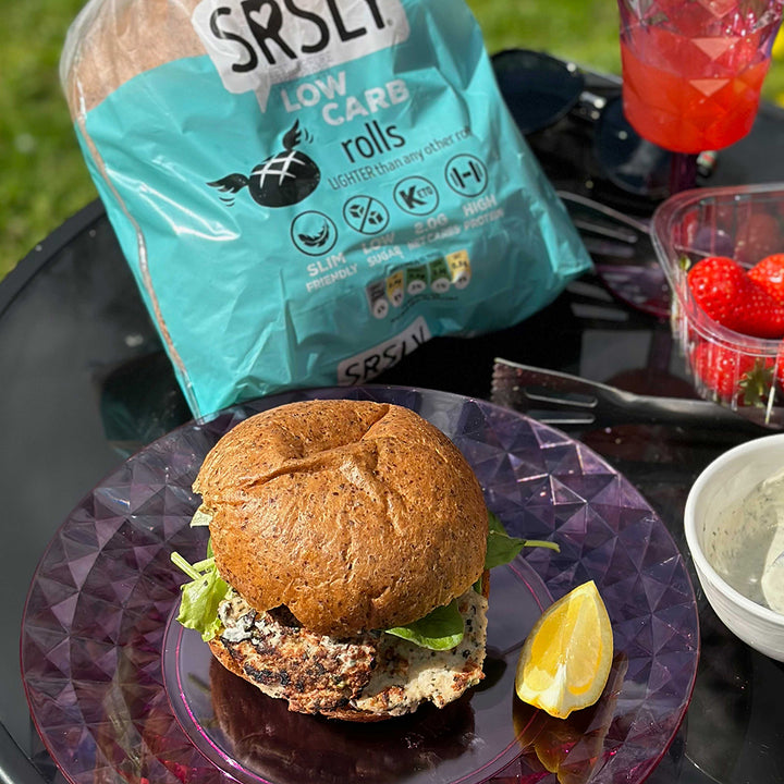 Picture - A delicious low carb bread roll on a glass table outside with a beef burger in it on a sunny day