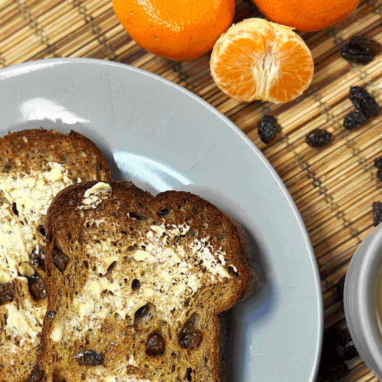 Picture - Toasted buttered fruit bread with the butter just starting to melt, surrounded by oranges and sultanas. 