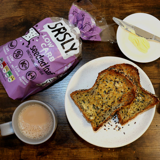 Picture - Low carb seeded bread toasted and slathered in butter next to a piping hot cup of tea. 