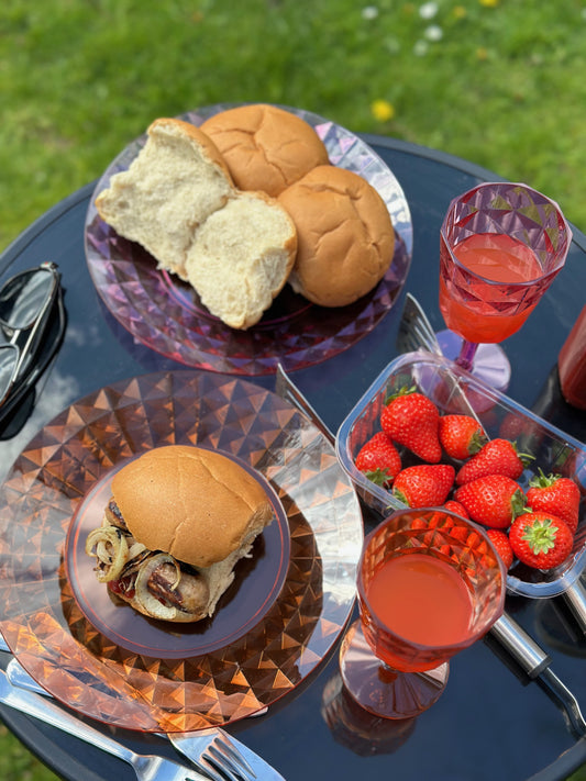 Picture - Keto friendly white rolls on a garden table on a sunny day. The rolls are filled with sausages and onion, accompanied by a glass of fizz for an awesome low carb BBQ. 